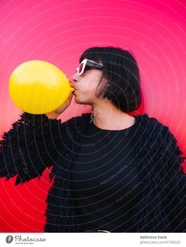 Trendy Frau bläst Ballon gegen roten Hintergrund Schlag Luftballon ausgefallen cool urban lebhaft trendy Farbe Outfit Mode Sonnenbrille Straße Großstadt Stil