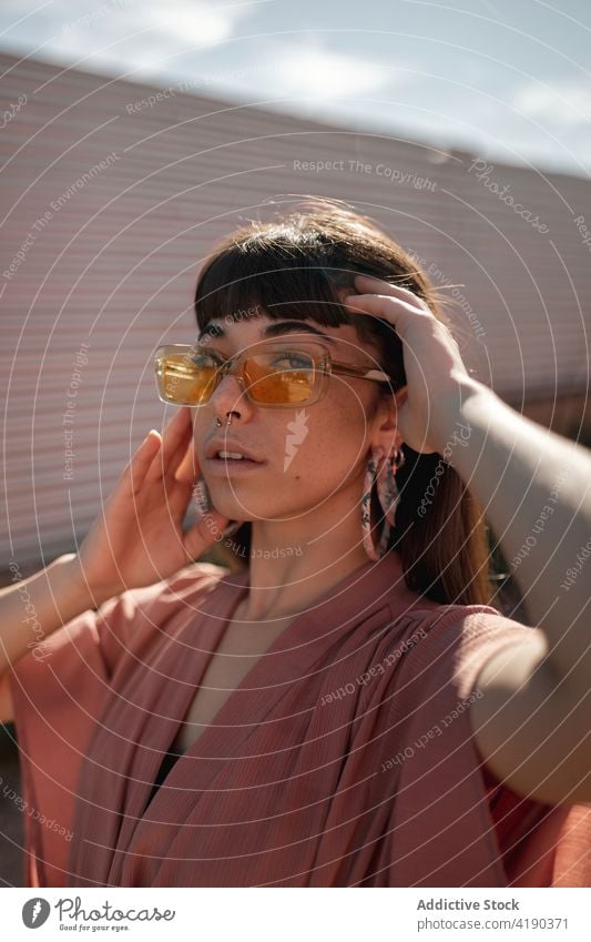 Modische junge ethnische Dame steht in der Nähe der Wand und schaut in die Kamera Frau besinnlich nachdenklich Stil cool Mode Windstille Straße verträumt