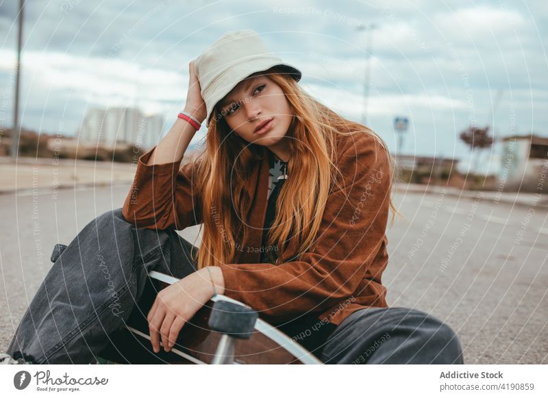 Ernsthafte junge Millennials mit Skateboard in der Hand auf der Straße sitzend Frau Landschaft Skater ernst selbstbewusst Aktivität trendy Hobby Sport Natur