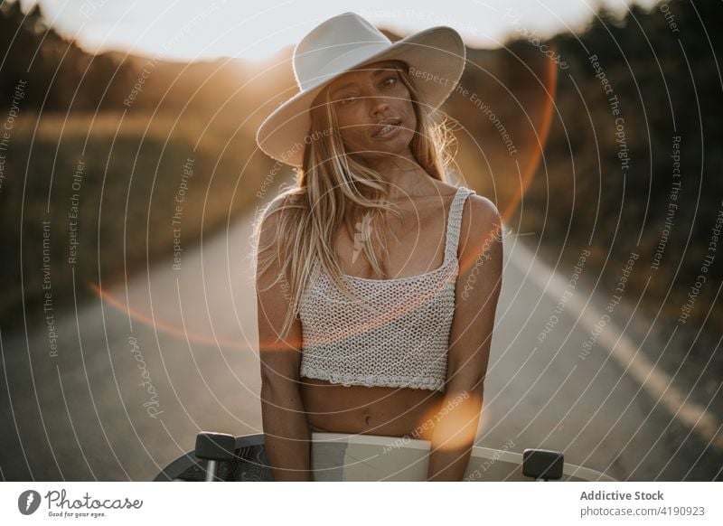 Attraktive Frau mit Cruiser-Board steht auf einer leeren Landstraße Skater Straße Holzplatte ländlich Skateboard Sonnenuntergang Stil sportlich Fahrbahn Asphalt