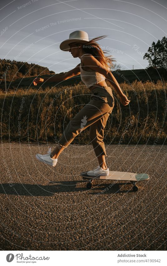 Stilvolle Frau beim Schlittschuhlaufen auf leerer Landstraße Skater Mitfahrgelegenheit Cruiser Straße ländlich aktiv Energie Skateboard Gleichgewicht Fahrbahn