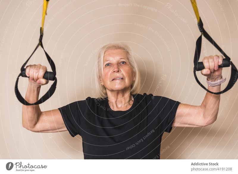 Ältere Sportlerin trainiert mit Riemen auf hellem Hintergrund Athlet Gurt Fahrwerkstraining Training üben Gesunder Lebensstil Übung Frau Porträt Fitnessstudio