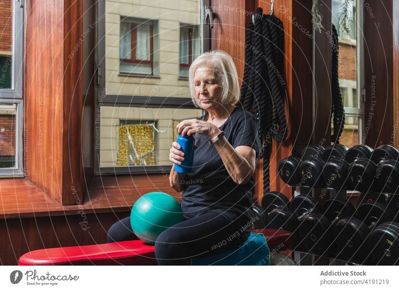 Ältere Sportlerin öffnet Wasserflasche beim Training im Fitnessstudio Athlet offen Flasche Pause Gerät Frau Sporthalle Übung Ball klein Bank ruhen