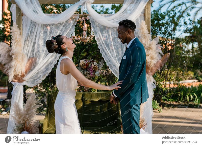 Fröhliches frisch verheiratetes Paar, das sich im Garten umarmt Jungvermählter Umarmung heiter Braut striegeln Hochzeit Liebe Zusammensein multiethnisch