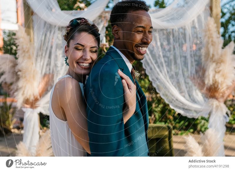 Fröhliches frisch verheiratetes Paar, das sich im Garten umarmt Jungvermählter Umarmung heiter Braut striegeln Hochzeit Liebe Zusammensein multiethnisch