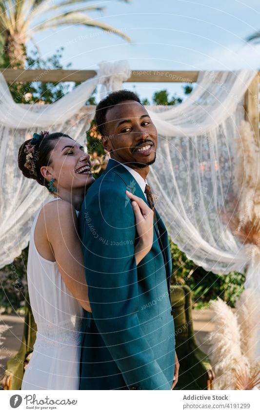 Fröhliches frisch verheiratetes Paar, das sich im Garten umarmt Jungvermählter Umarmung heiter Braut striegeln Hochzeit Liebe Zusammensein multiethnisch