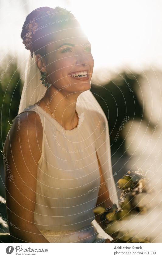 Fröhliche Braut mit Blumenstrauß im Garten hochzeitlich heiter charmant Hochzeit weißes Kleid Jungvermählter Frau Sommer ausgefallen Veranstaltung elegant