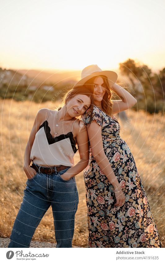 Fröhliche Freunde in stilvollem Outfit stehen im Feld in sonnigen Tag Frauen schwanger Landschaft Natur positiv charmant heiter Sonnenlicht Stil mütterlich froh