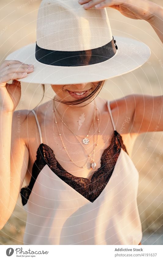 Glückliche Frau mit Hut im Feld stehend Lächeln heiter deckend versteckend Gesicht positiv Stil Landschaft Natur Optimist Zahnfarbenes Lächeln Gras trocknen