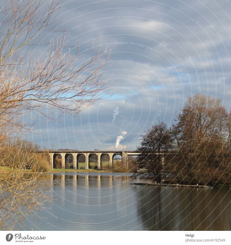 Viadukt am See mit Spiegelung, im Hintergrund hohe rauchende Schornsteine Brücke Obersee Bielefeld Rauch Seeufer Baum Strauch Himmel Wolken Landschaft Natur