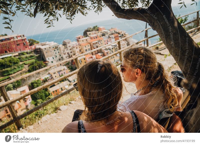 Zwei junge Frauen unterm Olivenbaum mit Blick auf Manarola blond Sonne Sonnenlicht Baum Portrait lächeln schön hübsch Urlaub Sommer Sommerfeeling Außenaufnahme