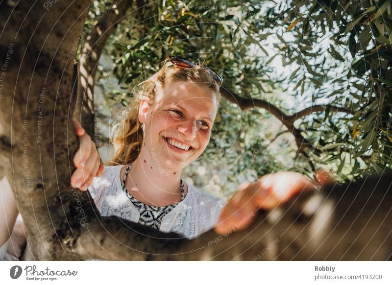 Lächelnde junge Frau unterm Olivenbaum blond Sonne Sonnenlicht Baum Portrait lächeln schön hübsch Urlaub Sommer Sommerfeeling Außenaufnahme Farbfoto Freude