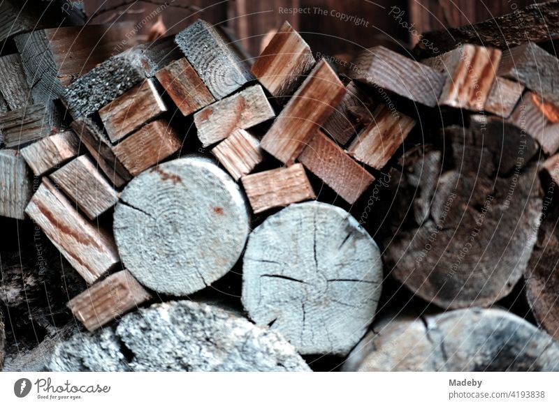 Holzstapel mit Rundholz und Kantholz für den Kamin vor einer alten Scheune auf einem Bauernhof in Rudersau bei Rottenbuch im Kreis Weilheim-Schongau in Oberbayern