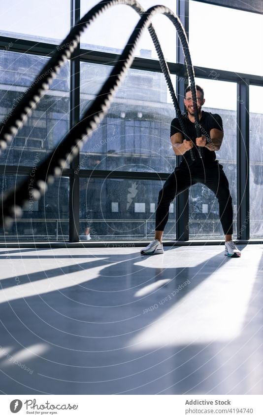 Aktiver Mann beim Training mit Kampfseilen im Fitnessstudio Sportler Athlet Seil Ausdauer anstrengen stark Kraft intensiv Schlacht Übung Wohlbefinden Motivation