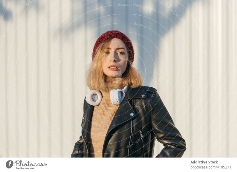 Stilvolle Frau mit Kopfhörern auf der Straße Wegsehen von unten Streetstyle Outfit urban cool trendy Großstadt Bestimmen Sie unabhängig stehen selbstbewusst