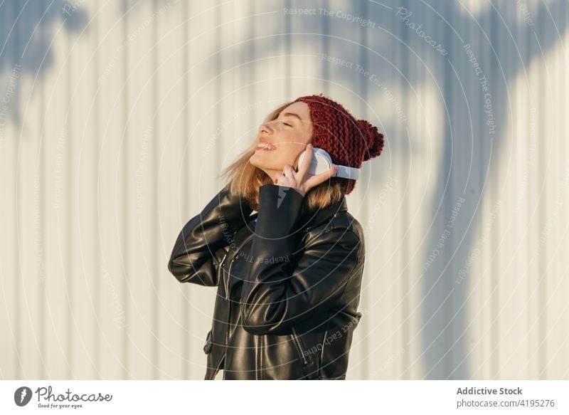 Stilvolle Frau mit Kopfhörern auf der Straße Wegsehen von unten Streetstyle Outfit urban cool trendy Großstadt Bestimmen Sie unabhängig stehen selbstbewusst