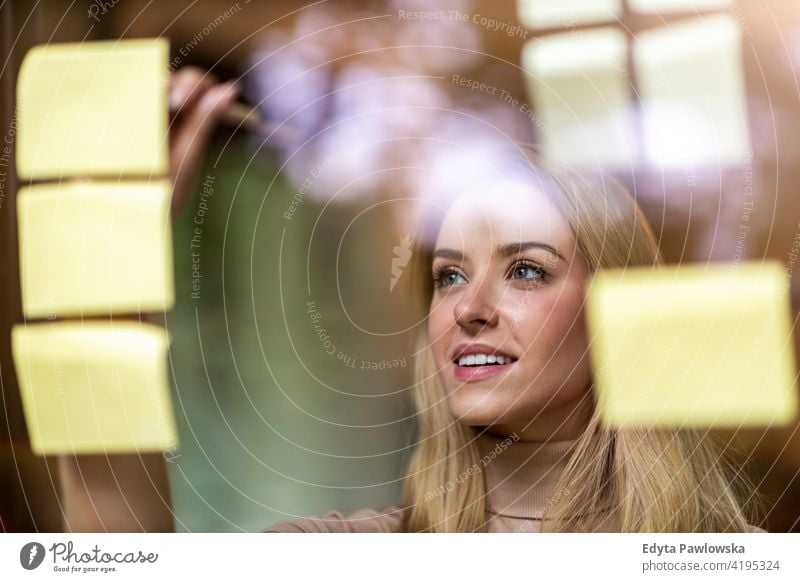 Junge Geschäftsfrau beim Brainstorming mit Notizen an einer Glaswand in einem Büro Frau Mädchen Menschen Unternehmer Business gelungen Erfolg professionell jung