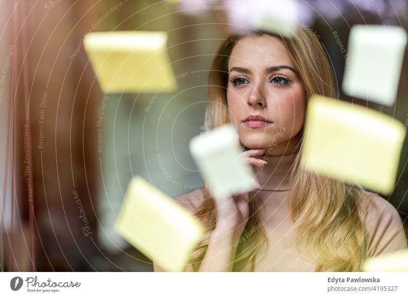 Junge Geschäftsfrau beim Brainstorming mit Notizen an einer Glaswand in einem Büro Frau Mädchen Menschen Unternehmer Business gelungen Erfolg professionell jung