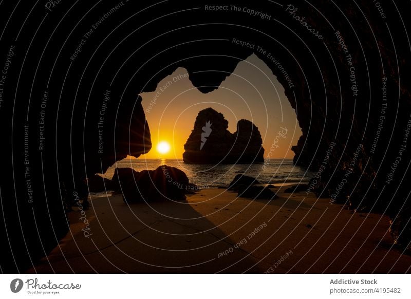 Felsige Klippe in wogenden Meer in der Nähe von Sandstrand bei Sonnenuntergang Strand Höhle Natur Landschaft Meereslandschaft idyllisch malerisch Algarve