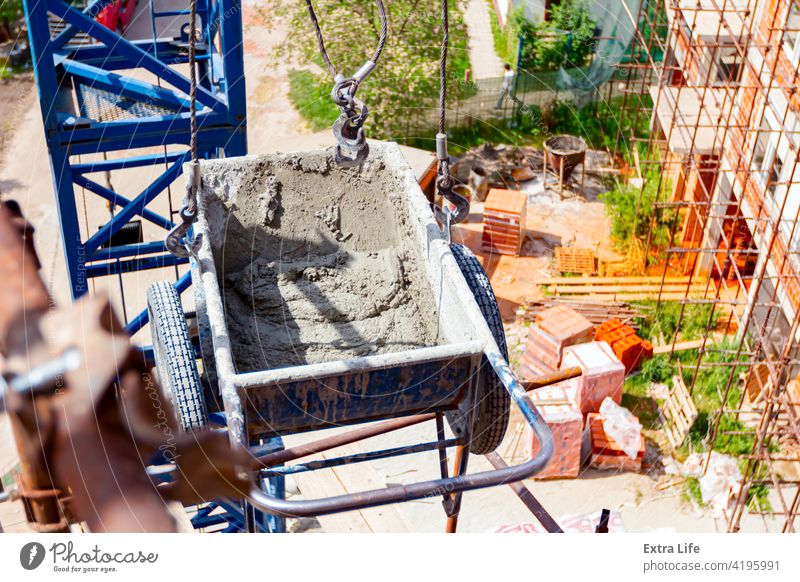 Kran hebt industrielle Kippschubkarre über Baustelle oben Aktivität Architektur Schubkarre Mauerwerk Träger führen Karre Zement Tiefbau Beton betonieren