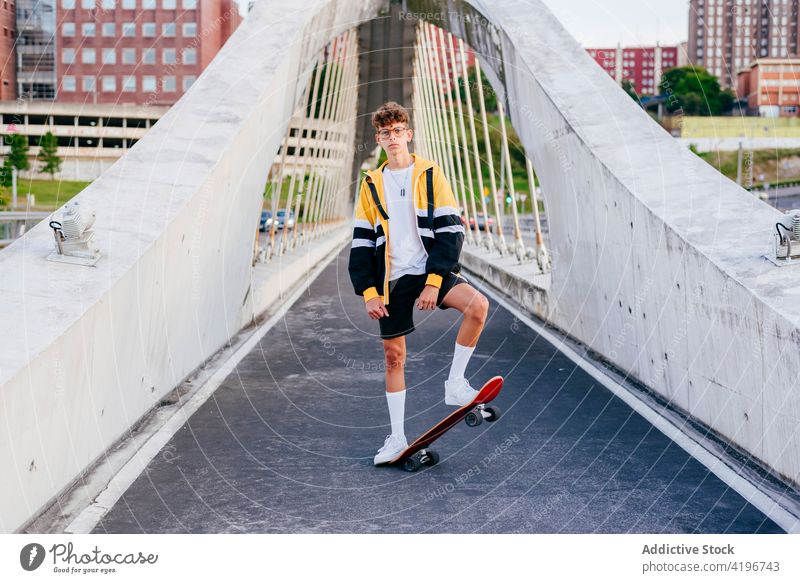 Kaukasischer Teenager mit Skateboard auf der Brücke in der Stadt stehend Herbst blond Junge Kaukasier Großstadt farbenfroh selbstbewusst Tageslicht horizontal