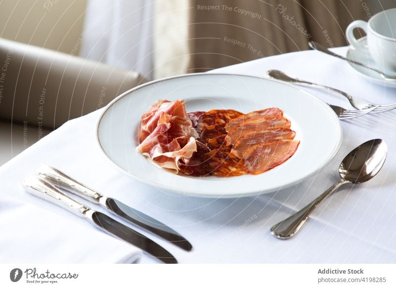 Gemischte Schinkenscheiben in einem Teller, der beim Frühstück auf dem Tisch steht Kaffee Besteck Fleisch Jamón Chorizo Restaurant lecker sortiert geschmackvoll