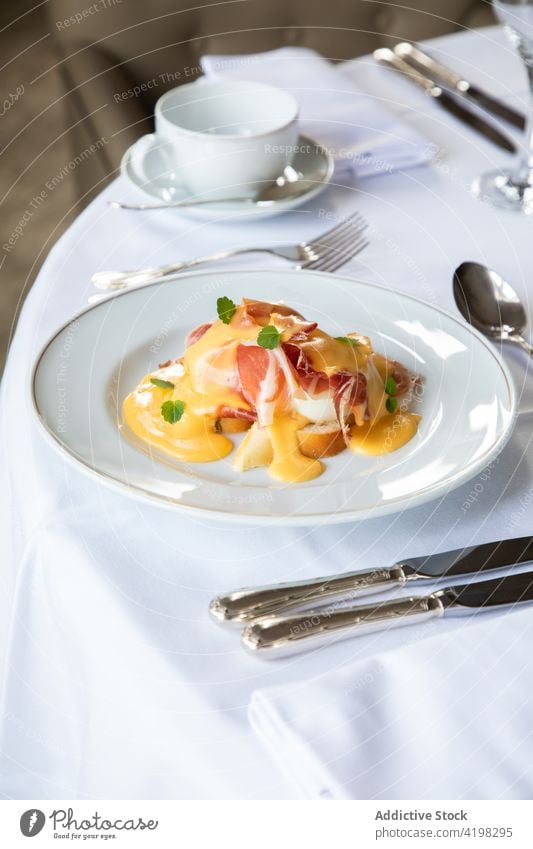 Leckeres pochiertes Ei mit Speck und Soße, das beim Frühstück auf dem Tisch serviert wird Benedikt Saucen Kaffee Silberwaren Brunch appetitlich Speise Mahlzeit