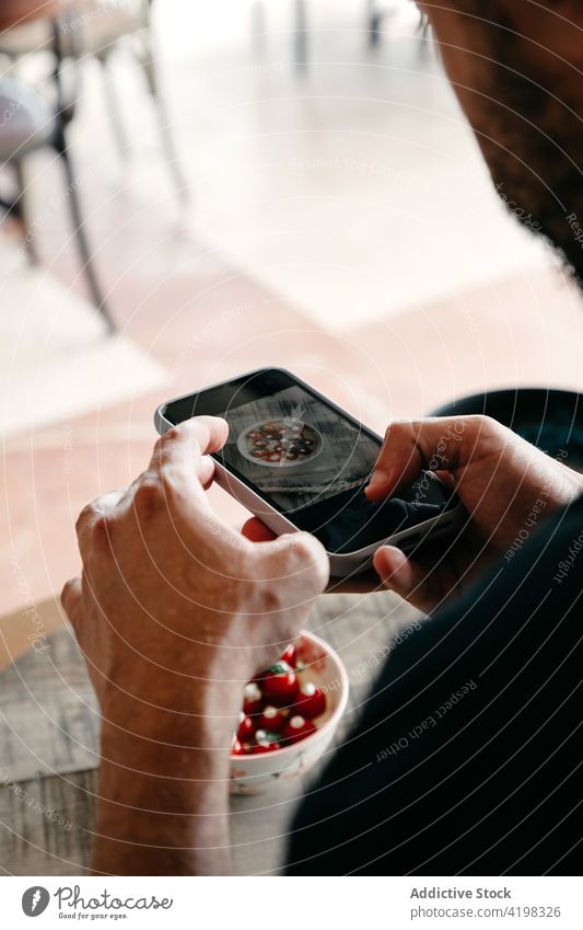 Anonymer Koch benutzt Smartphone, um Essen in Schüssel zu schießen Mann Küchenchef benutzend fotografieren kulinarisch Mahlzeit Restaurant Speise männlich