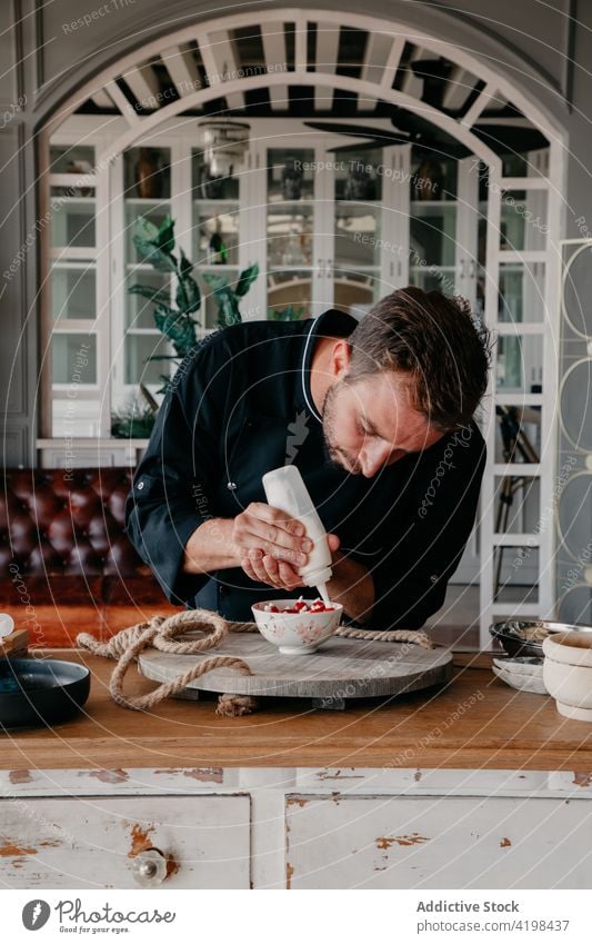 Konzentrierter Mann dekoriert Dessert mit Sahne in einem stilvollen Restaurant dekorieren Küchenchef Beeren lecker Koch Konzentration Job kulinarisch