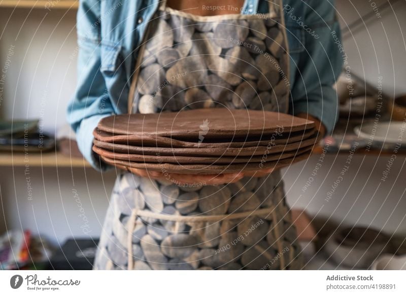 Anonyme Töpferin mit flachen Tonstücken in der Werkstatt Frau Teller Tonwaren Arbeit Kunstgewerbler Handarbeit kreativ Fähigkeit Handwerk Basteln lässig Schürze