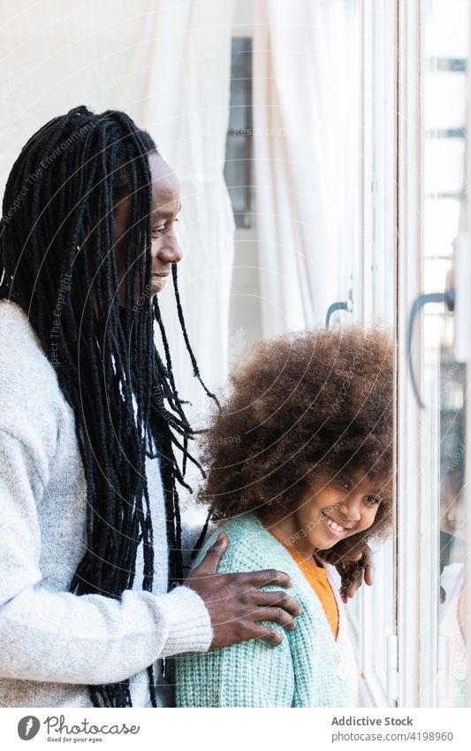 Schwarzer Vater mit Tochter steht am Fenster schließen heiter sorgenfrei Bonden positiv Angebot Lächeln Umarmung Mädchen Mann Papa Kindheit Afro-Look Eltern