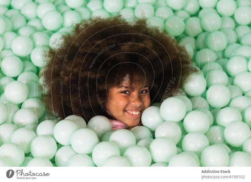 Fröhliches Kind im Bällebad Grube Ball spielen heiter Pool Kunststoff Glück Afro-Look Frisur ethnisch schwarz Afroamerikaner Spaß Kindheit Spaß haben genießen