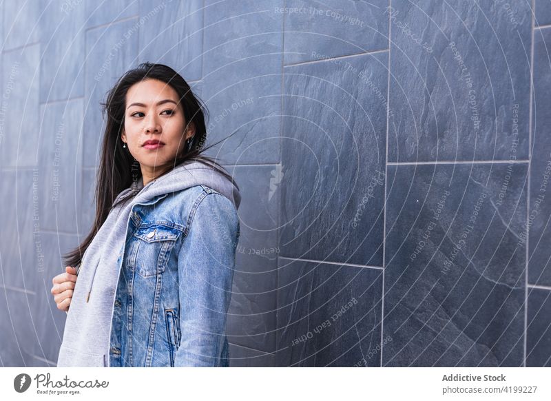 Asiatische brünette Frau mit langen Haaren lehnt an der Wand und schaut weg Japanisch asiatisch Asien jung Model Chinesisch Stil attraktiv Dame Straße modern