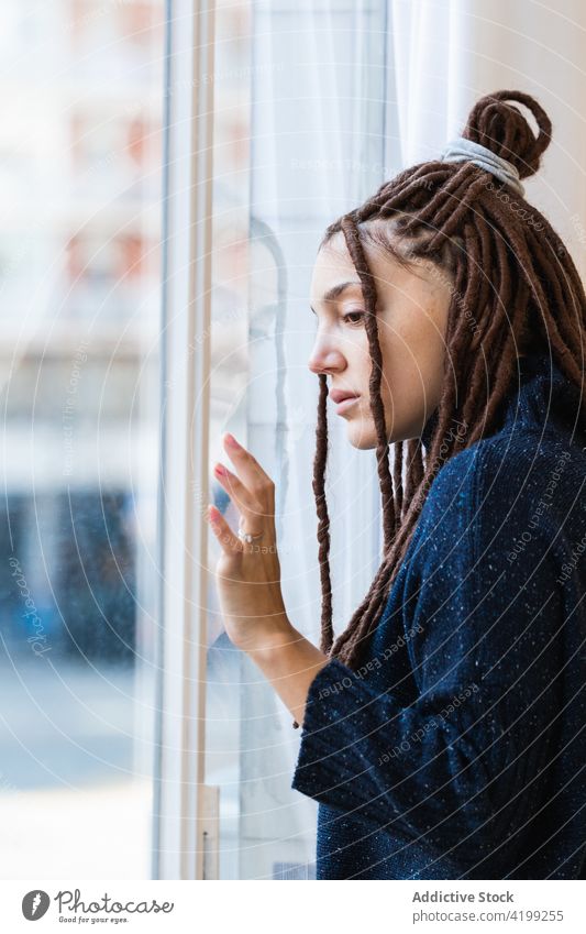 Nachdenkliche Frau mit Dreadlocks schaut aus dem Fenster besinnlich heimwärts Blick Menschen Denken Rastalocken Zopf Kontemplation schön Porträt Person