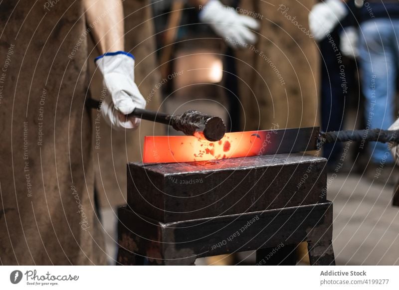 Schmied mit Handschuhen, der heiß auf ein Metallteil auf dem Amboss schlägt Mann Hufschmied bügeln Prozess aufschlagen Hammer Werkzeug herstellen männlich