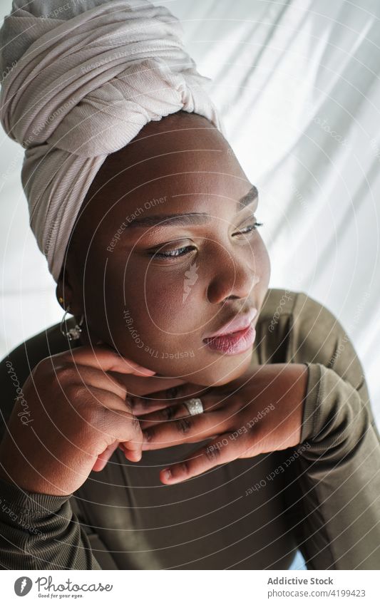 Selbstbewusste afrikanische Frau auf einem Stuhl sitzend mit den Händen am Kinn Hand am Kinn selbstbewusst Verlockung Stil feminin traumhaft Inhalt