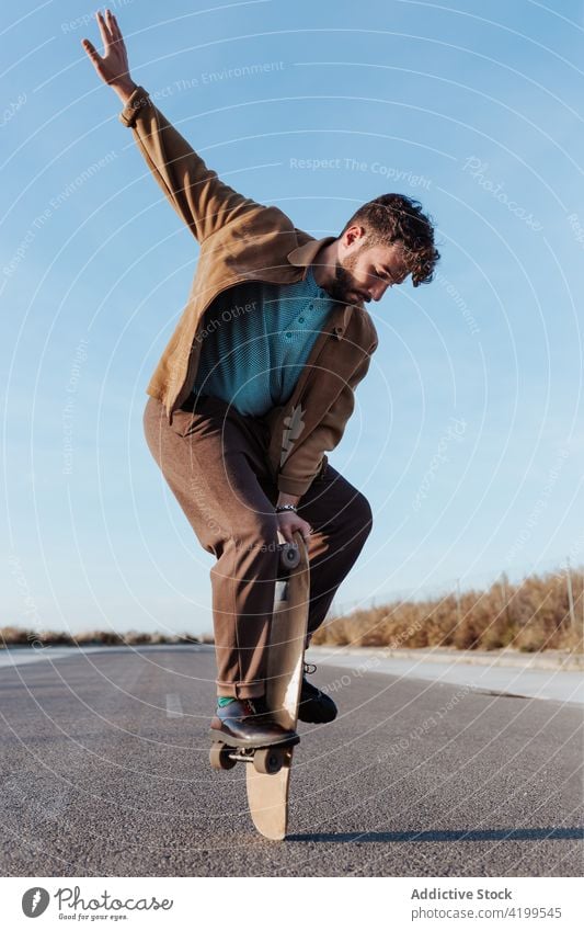 Trendiger Skater, der auf dem Skateboard stehend das Gleichgewicht hält Mann Trick Natur ausführen Saum Fähigkeit Landschaft ländlich Hobby Straße männlich