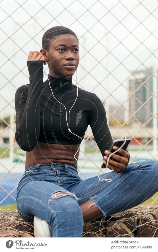 Kurzhaarige schwarze Frau, die mit einem Mobiltelefon und Kopfhörern Musik hört Afroamerikaner Smartphone Headset Gesang zuhören Kurze Haare Porträt benutzend