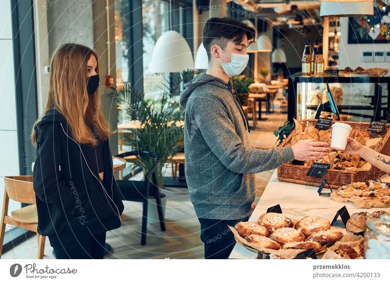 Menschen stehen in einer Warteschlange, um Kaffee und Gebäck im Coffee-Shop zu kaufen, um zu gehen. Mann nimmt Kaffeetasse von Barista. Menschen tragen die Gesichtsmasken, um eine Virusinfektion zu vermeiden