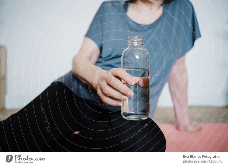 Nahaufnahme von reifen kaukasischen Senior Frau übt Yoga-Pose zu Hause. Sie hält eine Flasche Wasser. Gesunder Lebensstil trinken heimwärts Sport Gesundheit