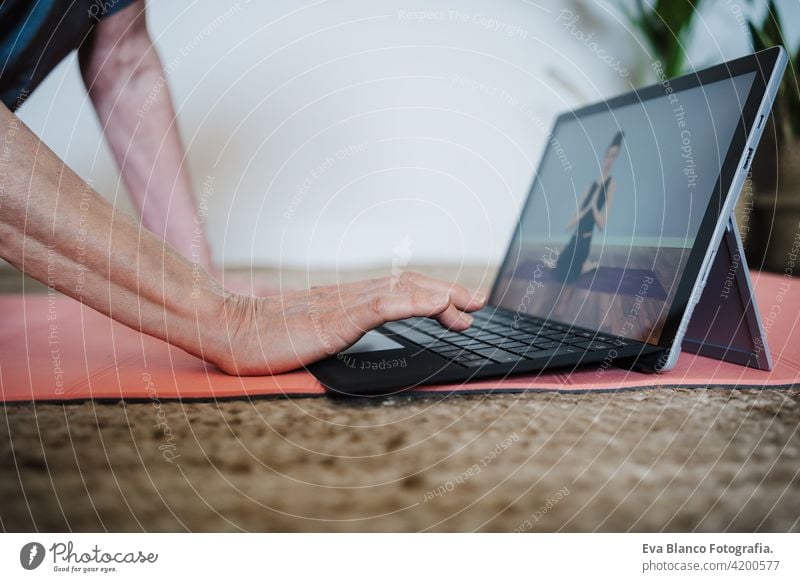 Nahaufnahme von reifen kaukasischen Senior Frau übt Yoga-Pose zu Hause. mit Laptop für Online-Klasse mit Lehrer. Gesunde und Technologie Lebensstil Seniorin