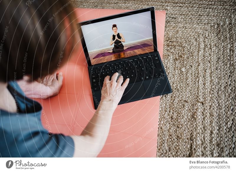 Nahaufnahme von reifen kaukasischen Senior Frau übt Yoga-Pose zu Hause. mit Laptop für Online-Klasse mit Lehrer. Gesunde und Technologie Lebensstil Seniorin