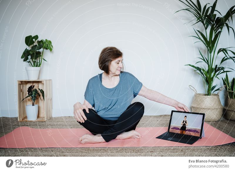 Nahaufnahme von reifen kaukasischen Senior Frau übt Yoga-Pose zu Hause. mit Laptop für Online-Klasse mit Lehrer. Gesunde und Technologie Lebensstil Seniorin