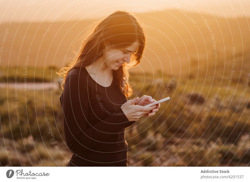 Zufriedene Frau mit Smartphone in den Bergen bei Sonnenuntergang Berge u. Gebirge Browsen Freiheit genießen Hochland Hügel heiter Internet online Gerät Telefon