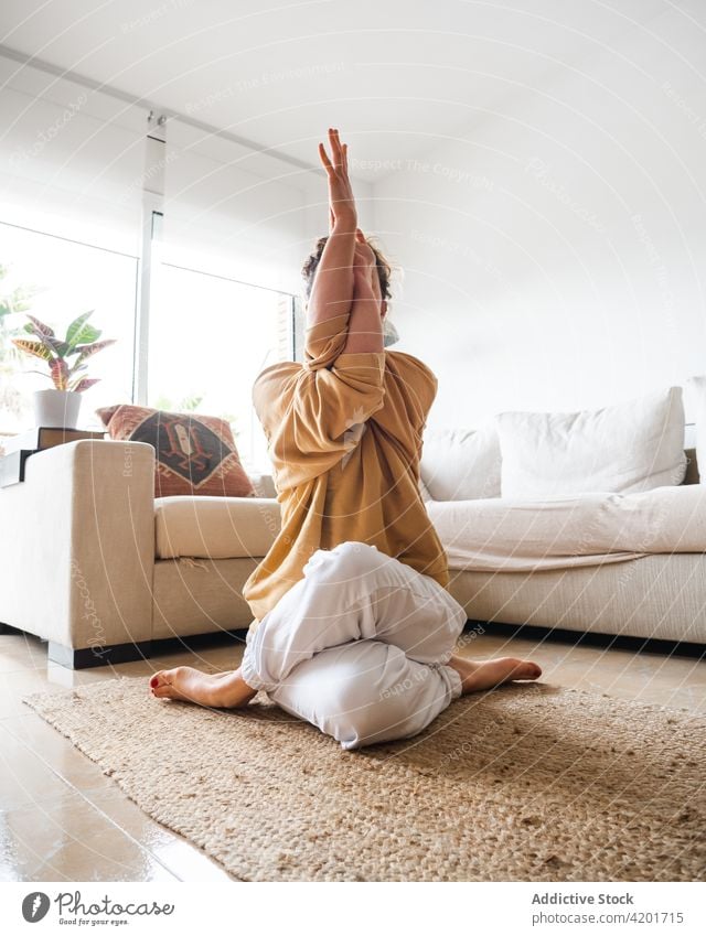 Frau sitzt auf dem Boden und macht Eagle Pose während Yoga-Sitzung Windstille Asana Adler-Pose Konzentration Aktivität garudasana Harmonie Zen Sportbekleidung