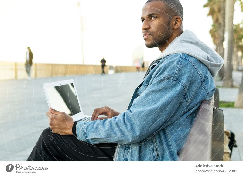 Schwarzer Freiberufler mit Laptop in der Stadt sitzend Mitarbeiter freiberuflich maskulin brutal Macho nachdenken Mann urban Netbook Arbeit Browsen praktisch