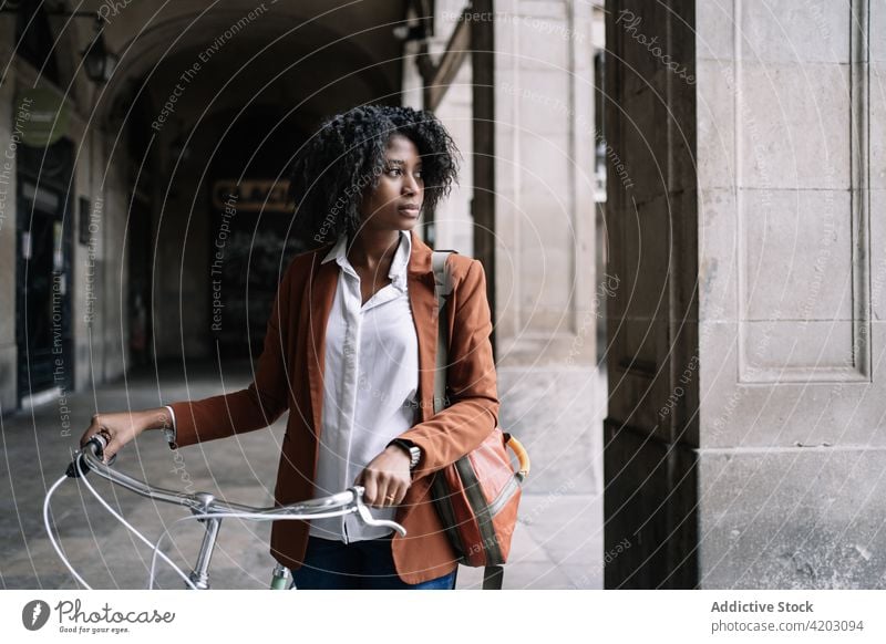 Ethnische Frau geht mit Fahrrad die Straße entlang Arbeitsweg Großstadt smart lässig Spaziergang trendy Stil schwarz Afroamerikaner ethnisch urban Zeitgenosse