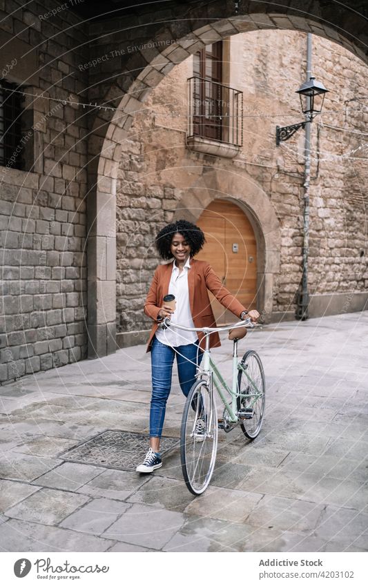 Ethnische Frau geht mit Fahrrad die Straße entlang Arbeitsweg Großstadt Spaziergang trendy schwarz Afroamerikaner ethnisch urban Zeitgenosse Fahrzeug Stadt