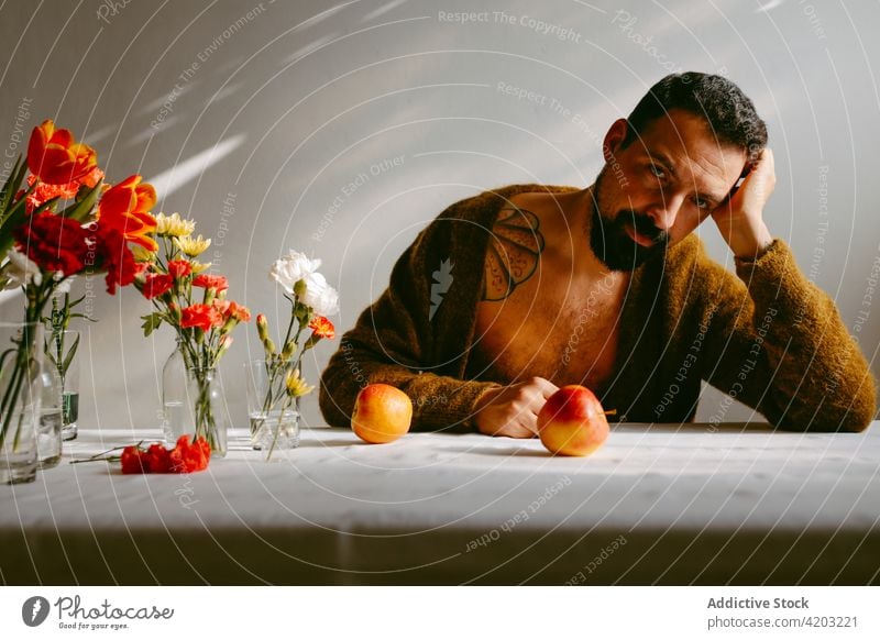 Nachdenklicher Mann mit frischen Blumen im Glas auf dem Tisch Tulpe reif Apfel nachdenklich Blumenstrauß Blüte männlich nachdenken Nelke Vollbart Vorbau Pflanze