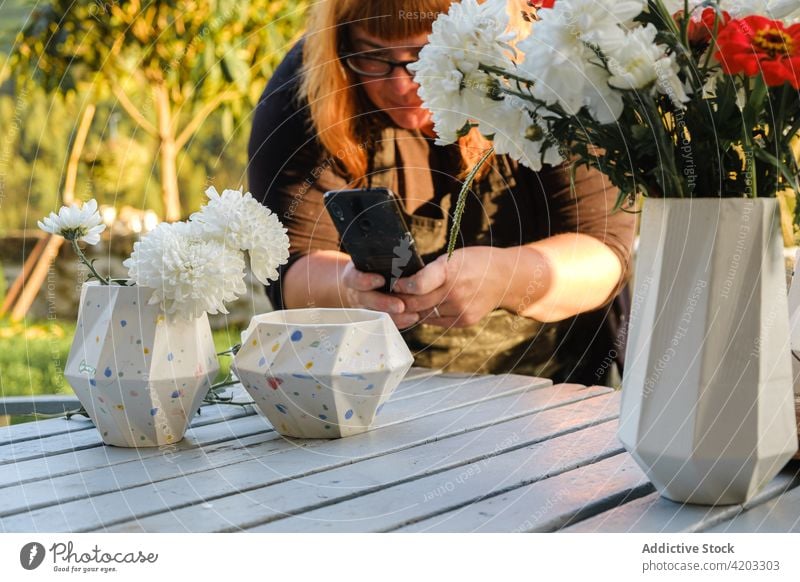 Frau fotografiert Vasen auf einem Tisch im Hof Smartphone fotografieren Blume Flora Fotografie Pflanze einfangen lässig Schürze benutzend Keramik sonnig Sommer